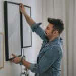man with beard hanging a painting on the wall at his living room