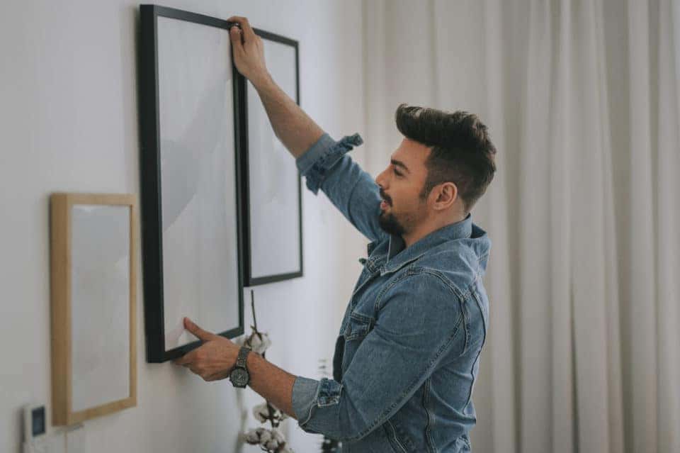 man with beard hanging a painting on the wall at his living room
