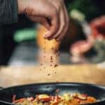 Sprinkling ground red chili pepper over sliced vegetables