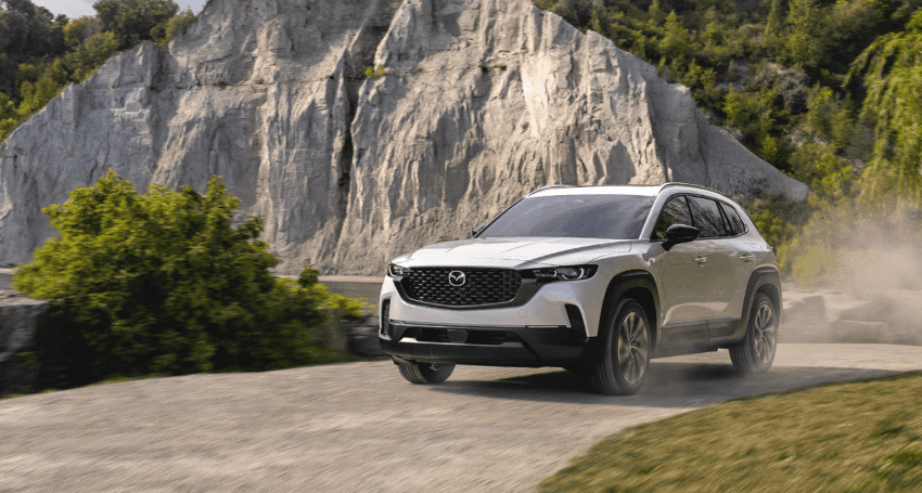 A White 2026 MAZDA CX-50 Hybrid driving past mountain.
