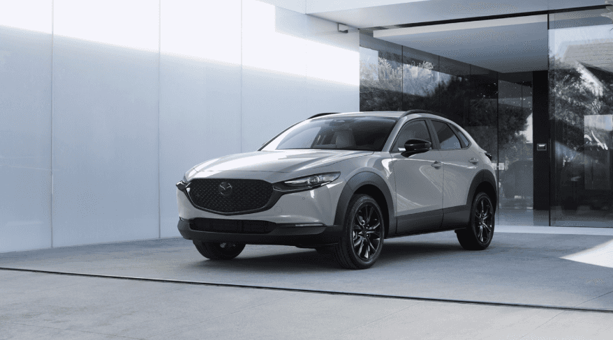 Light grey 2026 MAZDA CX-30 parked outside glass building.