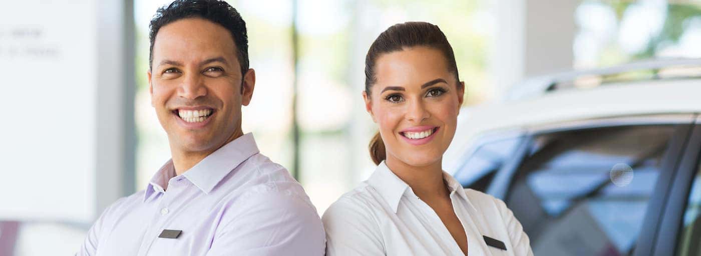 portrait of happy sales staff standing in vehicle showroom