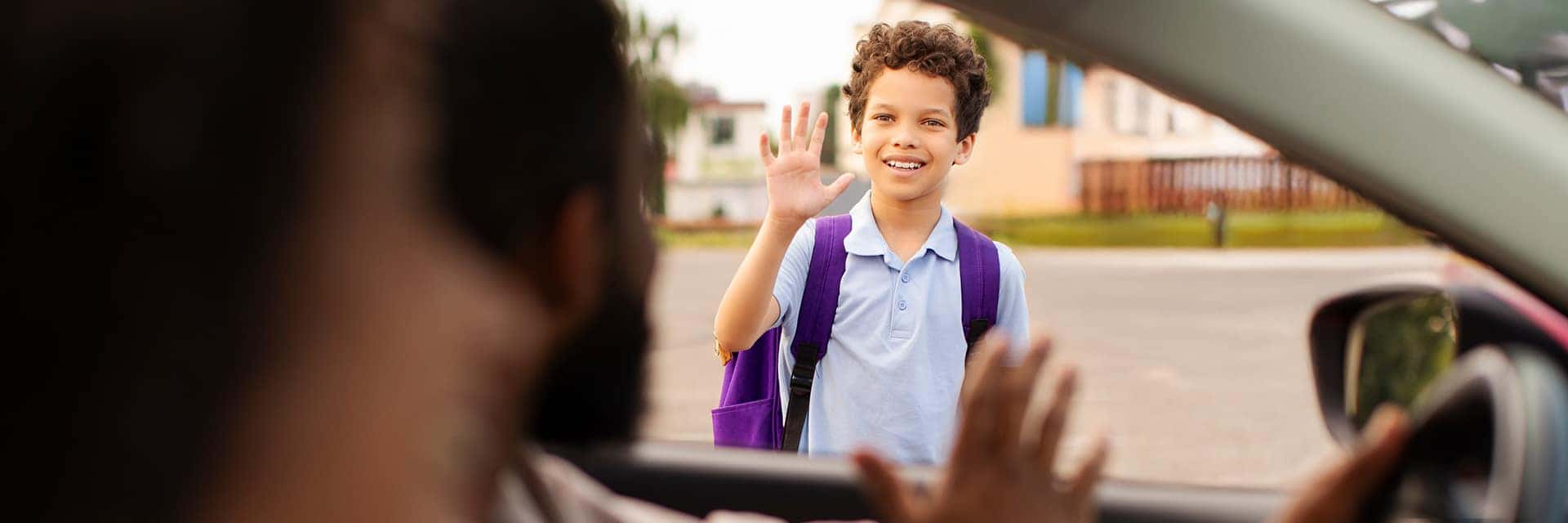 student waving to parents in car