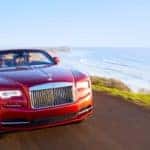 A Rolls-Royce Dawn driving down a road with an ocean view on the background
