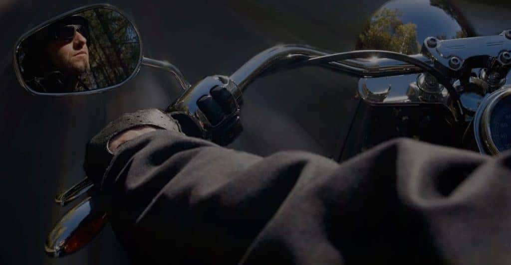 closeup looking over shoulder of Harley Davidson rider with his side profile caught in the side mirror