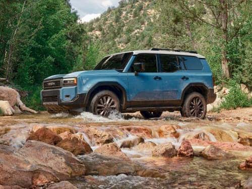 2024 Toyota Land Cruiser side view of vehicle driving across a rocky stream