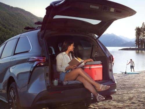 2024 Toyota Sienna parked near a lake with back door open and woman sitting in cargo area reading a book