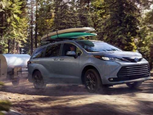 2024 Toyota Sienna driving down a dirt road towing a small enclosed trailer